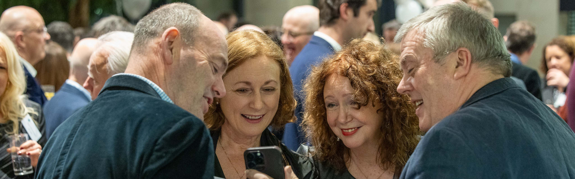 Four alumni at their reunion, looking at a phone screen and smiling.
